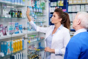 Beautiful young woman pharmacist showing drugs to senior man customer in pharmacy.